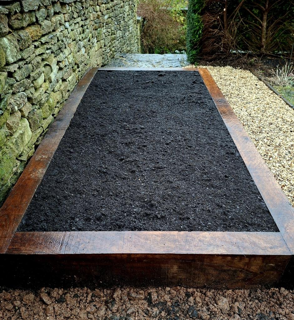 Timber-edged garden bed beside a dry-stone wall